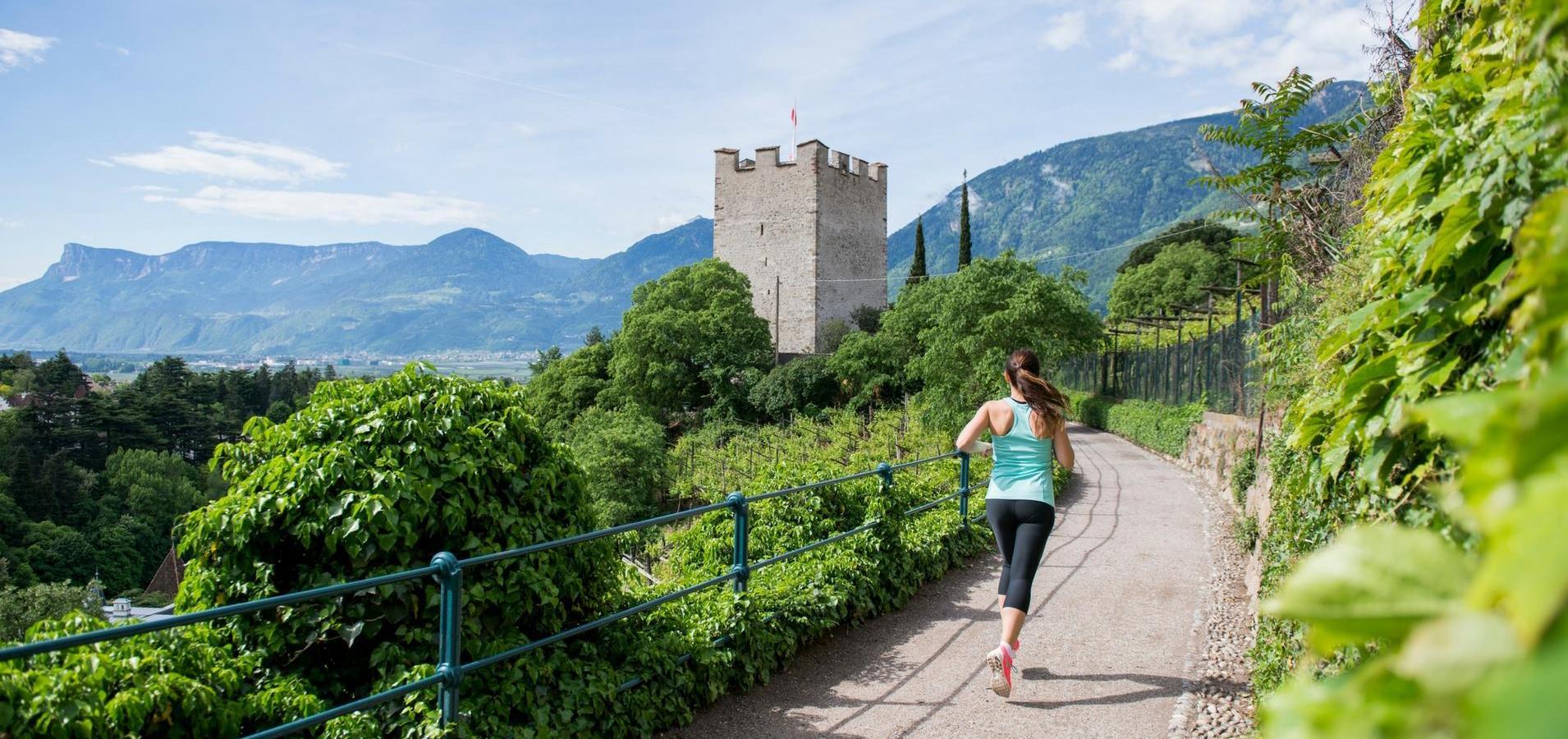 Una donna corre su un sentiero panoramico con vista su un castello e montagne.