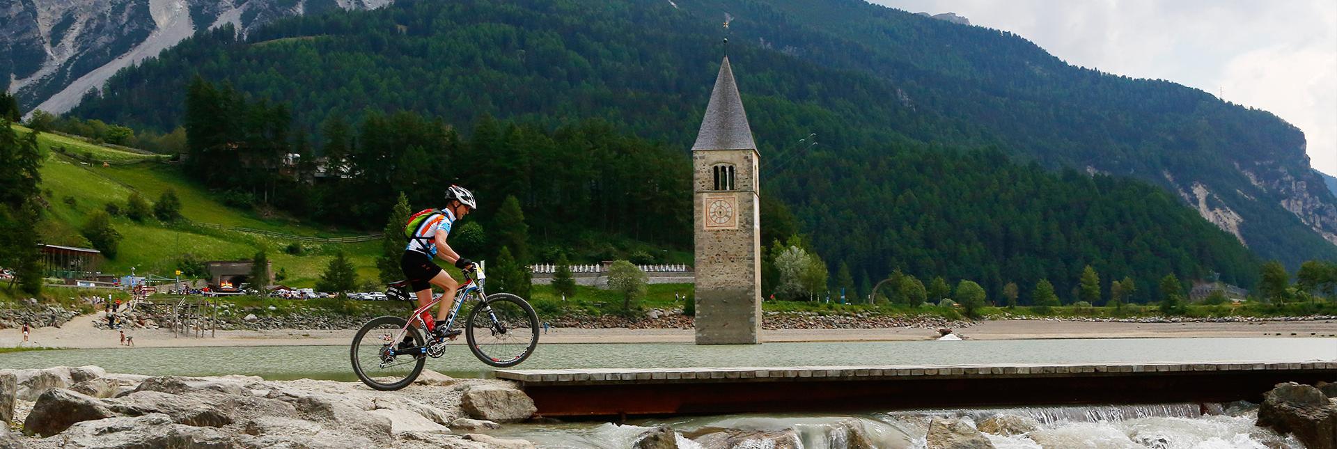 A cyclist rides past the submerged church tower in Lake Resia